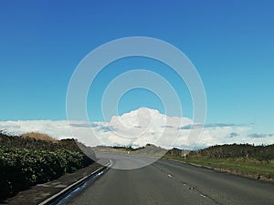 Open road with wide expanse of blue sky above with white clouds. The open road. Cycling tour.