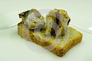 Open sandwich made of brown sprouted bread, slices of fillet of pickled Atlantic herring and green olives on a saucer closeup at