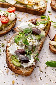 Open sandwich made of slices of sourdough bread with avocado, feta cheese, kalamata olives, olive oil and oregano on a wooden whit