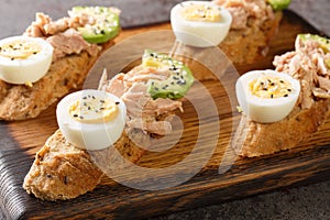 Open sandwiches with canned tuna, boiled egg, ripe avocado and sesame seeds close-up on a wooden board. Horizontal