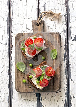 Open sandwiches with cream cheese,cherry tomatoes, green peas and basil close up