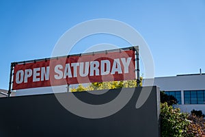 Open Saturday sign hanging on top of store building on sunny day photo