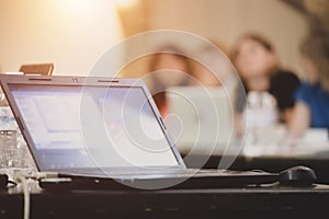 Open screen laptop in a conference room on the background of sitting people