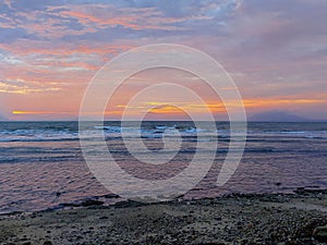 Open sea landscape with golden sunset sky in the distance and black sandy beach.