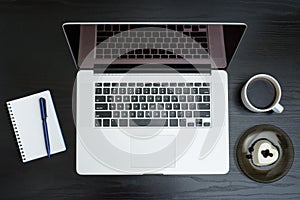 Open silver laptop, mug of coffee, note pad and dessert on a black background