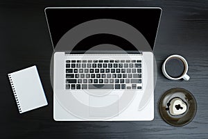 Open silver laptop, mug of coffee, note pad and dessert on a black background