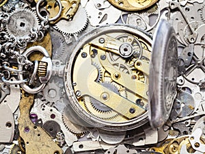 Open silver pocket watch on heap of spare parts