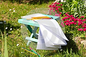 Open sketchbook, colored pencils and a folding chair for drawing on green grass