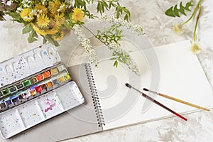 Open sketchbook, watercolor, brushes, and spring flowers above on the table. Leisure and hobbies concept