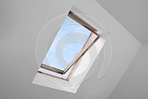 Open skylight roof window and lamps on slanted ceiling in attic room, low angle view