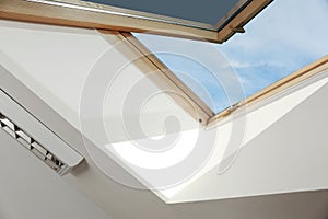 Open skylight roof window on slanted ceiling in attic room, low angle view