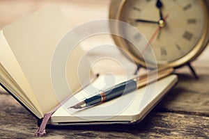 Open small notebook with fountain pen and old-fashioned alarm clock behind