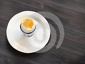 Open soft-boiled white egg in cup on plate on dark