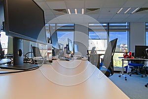 Open space empty modern office interior. Empty office desks and turned off computers and monitors against sunlight from windows.