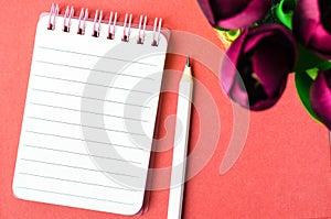 An open spiral bound notebook with lined paper and pencil with red tulip flower on red background