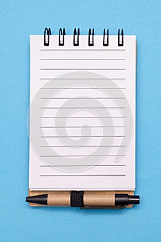 Open spiral lined paper notebook with small pen on blue background