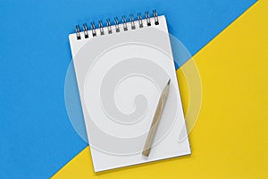 Open spiral notebook with a blank page and pencil on a blue and yellow background, with copy space