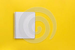 Open spiral squared notebook or notepad with blank empty white sheets and binder on bright yellow background, top view, flat lay