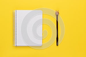 Open spiral squared notebook or notepad with blank empty white sheets and brown pen with bunny head on bright yellow background,