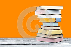 Open stacking book, hardback colorful books on wooden table and orange background. Back to school. Copy space for text. Education