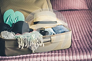 Open suitcase with female clothes for beach vacation.