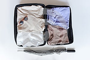 Open suitcase with female clothes for trip on white background