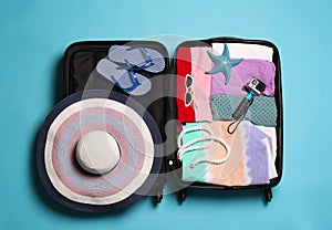 Open suitcase with traveler`s belongings on color background