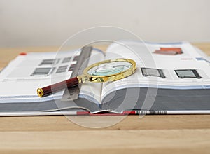 Open technical book for study with magnifying lens and ruler on wooden desk