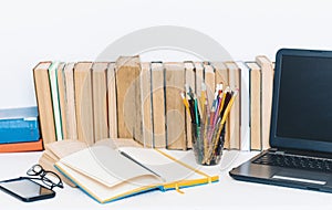 Open textbook, notebook, smartphone, laptop computer, stack of books education back to school background, glasses and pencils in