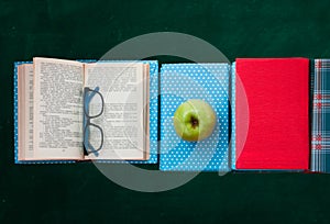 Open textbook  pile of books in colorful covers and apple with blackboard background. Distance home education. Back to school