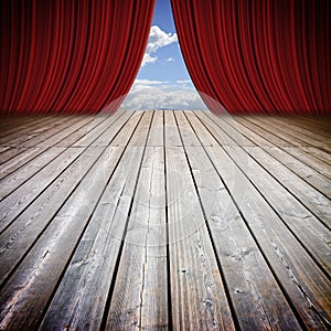 Open theater red curtains and wooden floor against a cloudy sky