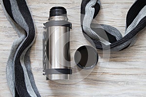 Open thermos flask and scarf on a woden background. Top view