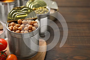 Open tin can with chickpeas and tomatoes on wooden table, closeup. Space for text