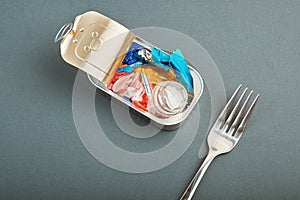 Open tin can and fork. Plastic waste instead of fish inside. Ocean plastic pollution concept