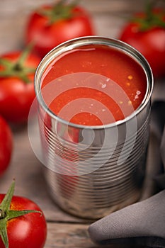 Open tin of tomatoes sauce with whole fresh tomatoes on a rustic wooden table