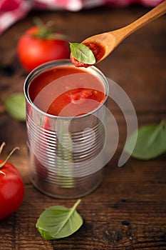 Open tin of tomatoes sauce with whole fresh tomatoes on a rustic wooden table