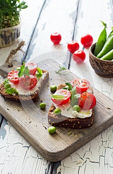 Open toasts with cream cheese, cherry tomatoes and green peas close up