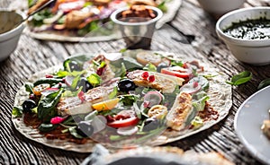 Open top vegetarian tortilla with salad, raddish, chery tomatoes, olives, pomegranate and grilled haloumi cheese