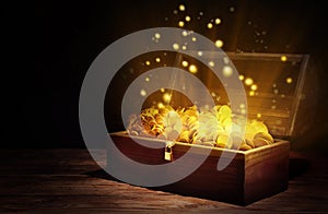 Open treasure chest with gold coins on wooden table against black background