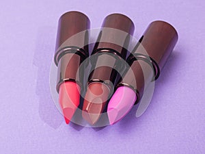 Open tubes of lipstick in different colors on a purple background