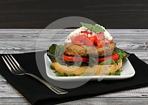 Open turkey burger garnished with chopped tomatoes, sauce, onions and basil
