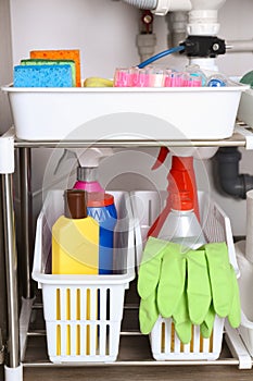 Open under sink cabinet with different cleaning supplies in kitchen