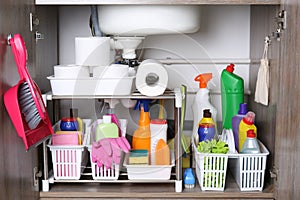 Open under sink cabinet with different cleaning supplies in kitchen