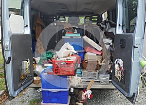 Open, untidy trunk of a delivery van, loaded with old tools, scrap and garbage