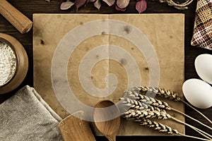 Open vintage book on the aged wooden background. Kitchen utensils, ears of wheat, flour in a pot. homemade, menu, recipe, mock