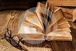 An open vintage book, glasses and a stack of old books on a vintage wooden table