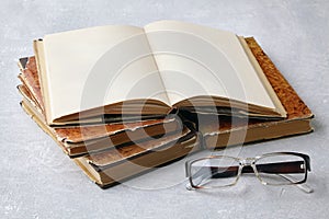 An open vintage book or notebook in a dust jacket on a stack of old shabby books and reading glasses