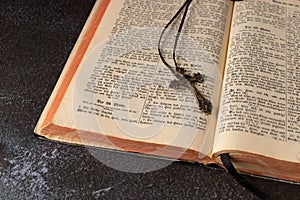 Open vintage holy bible with german text in old print and metal catholic cross with crucifix and ornament on dark grunge