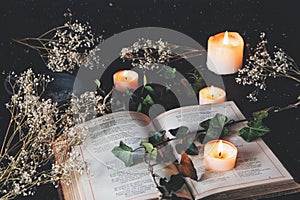 Open vintage poetry book on a black table surface with white lit burning candles and dried flowers