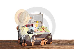 Open vintage suitcase with beach objects packed for summer vacation on wooden table against white background